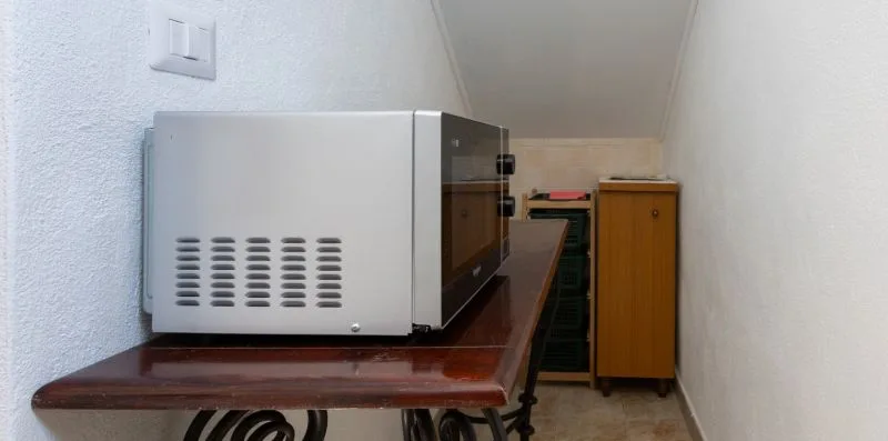A narrow kitchen area with a microwave on a counter and a wooden cabinet.