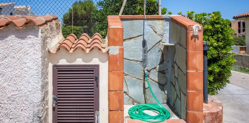 An outdoor shower with a green hose coiled on the tiled floor.