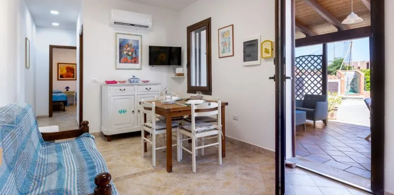 A dining area with a wooden table and chairs sits beside an open patio doorway.