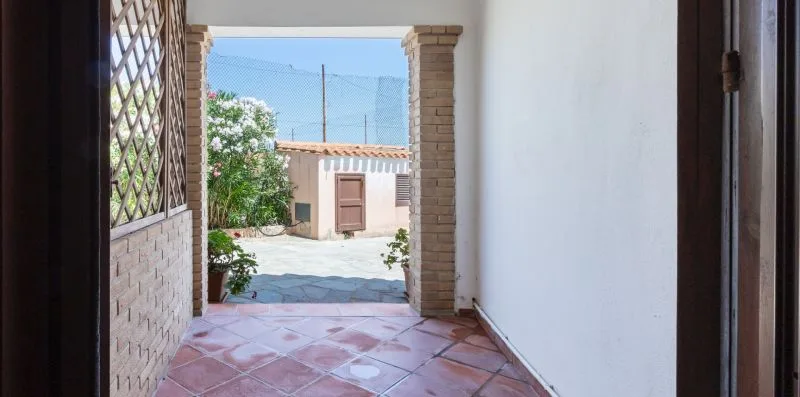 A tiled entryway opens onto a sunlit courtyard with a small outbuilding.