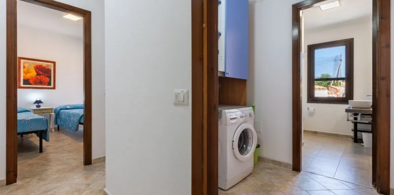 A hallway connects a bedroom, a laundry area, and a bright room with a desk.