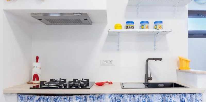 A bright kitchen with a stovetop, sink, and white countertops.