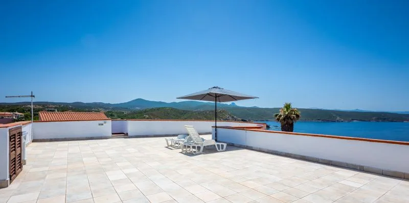 A spacious rooftop terrace overlooks the water, with lounge seating beneath a sun umbrella.