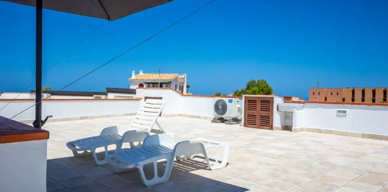 A sunny rooftop terrace with lounge seating and a clear blue sky.