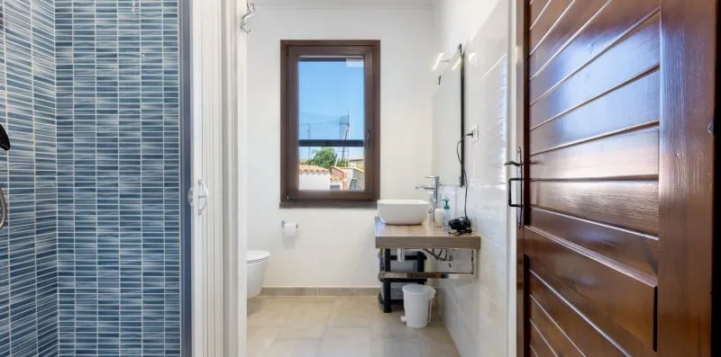 A bathroom with a tiled shower, sink, and window.