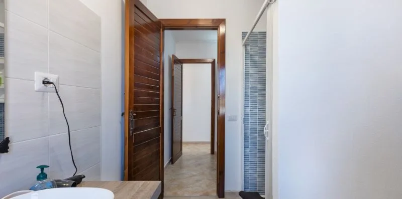 A tiled bathroom opens onto a hallway through a wooden doorway.