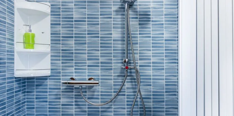 A tiled shower area with a wall-mounted showerhead and shelves.