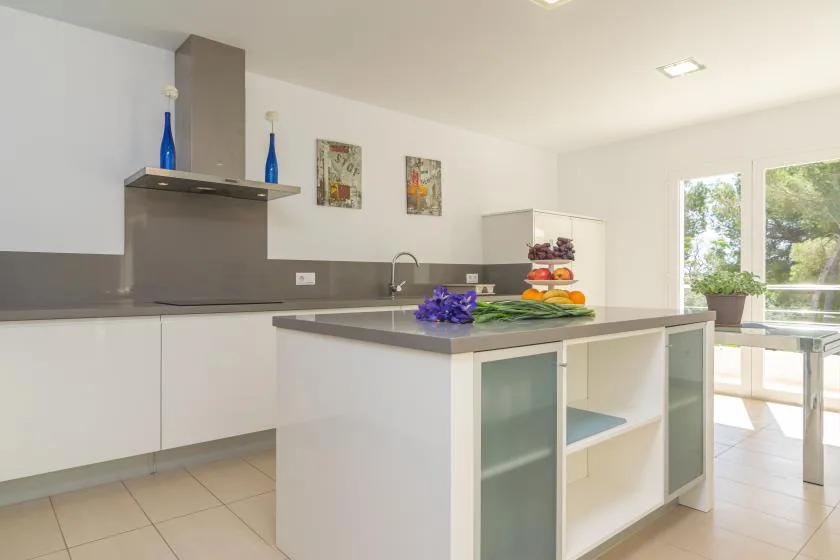 A bright modern kitchen with a central island and large windows.