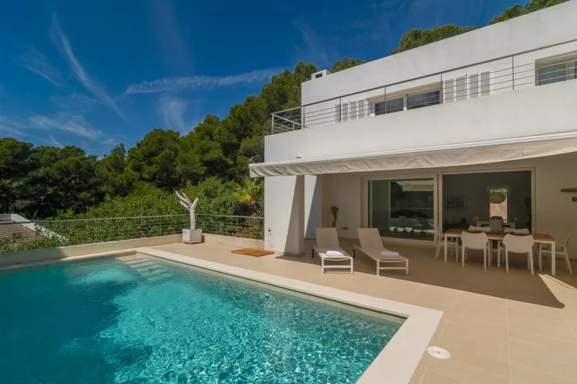 A modern house opens onto a swimming pool and patio with outdoor seating.