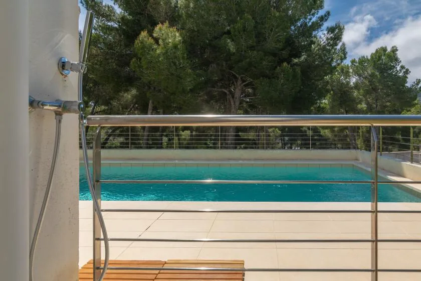 An outdoor swimming pool with a metal railing and trees beyond.