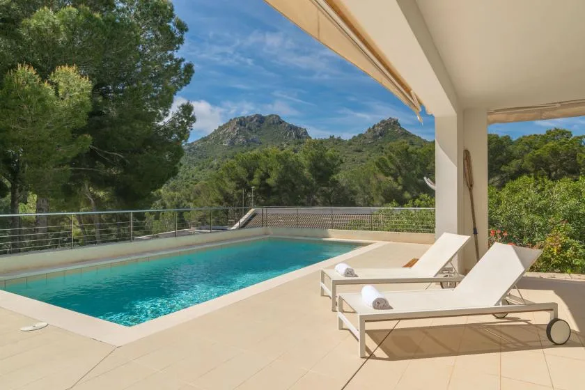 A swimming pool and sun loungers sit on a terrace overlooking green hills.