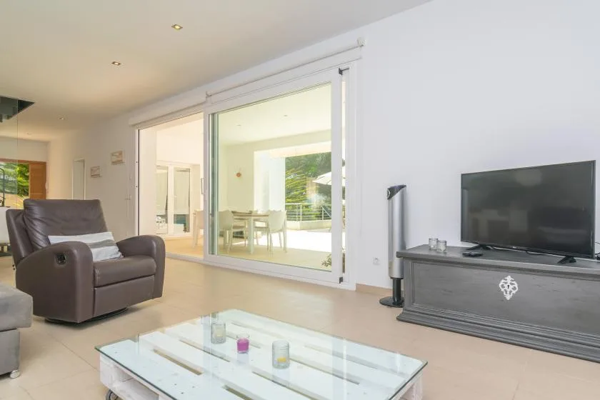 A bright living room has a glass coffee table and a television.