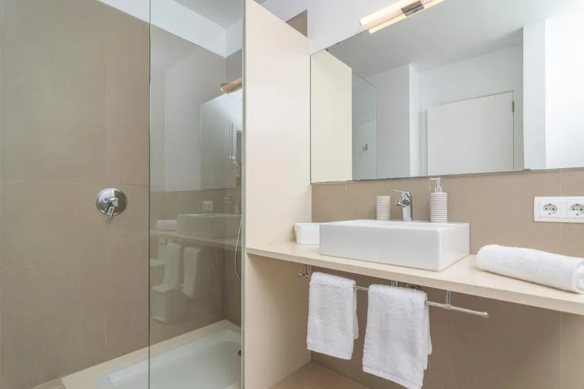 A bathroom vanity with a sink and mirror beside a glass shower.
