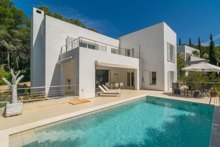 A modern white house opens onto a swimming pool and sunlit patio.