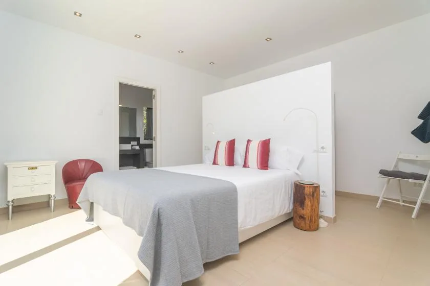 A bright bedroom with a bed, red accent pillows, and a small bedside table.