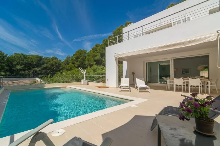 A swimming pool beside a modern white house and outdoor seating.