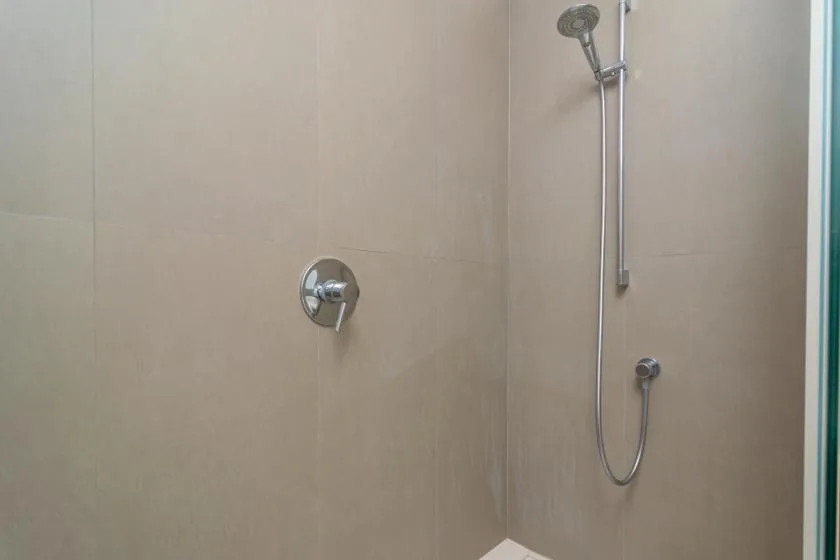 A tiled shower area with a handheld showerhead and wall controls.