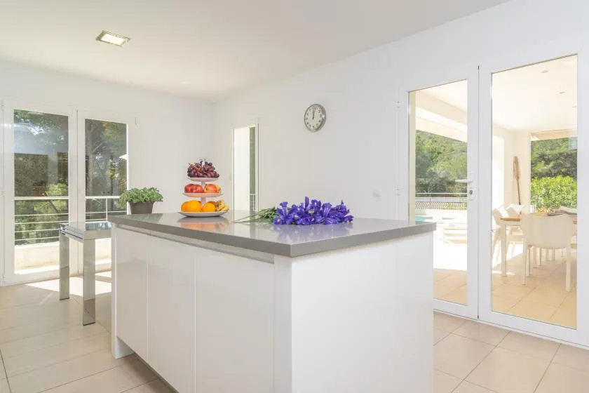 A bright kitchen with a central island, flowers, and fruit.