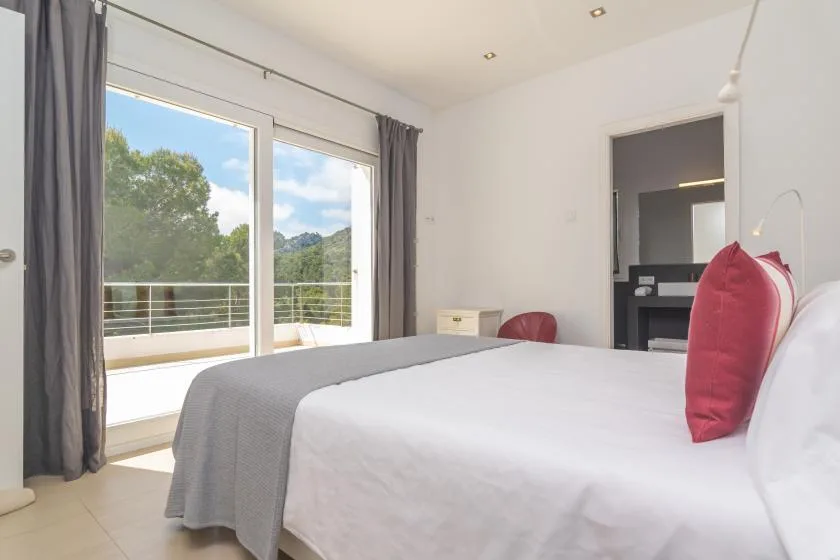 A bright bedroom with a bed beside sliding glass doors opening onto a balcony.