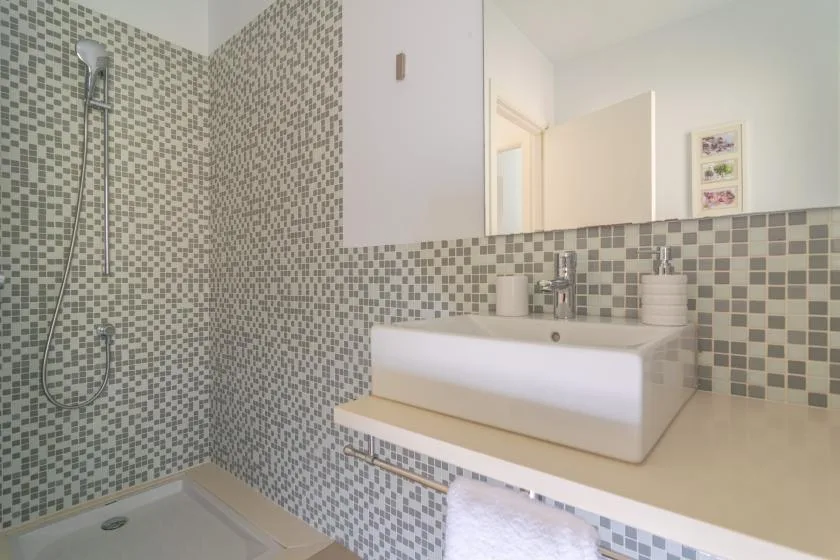 A tiled bathroom with a wall-mounted shower and a sink beneath a mirror.