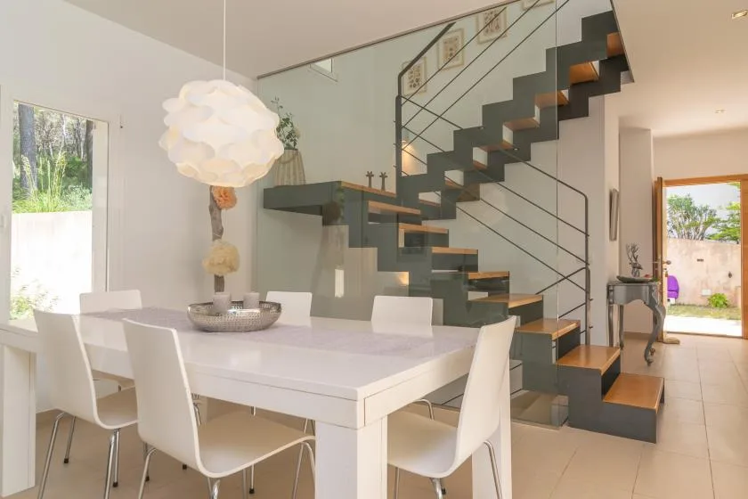 A bright dining area with a white table beneath a modern staircase.