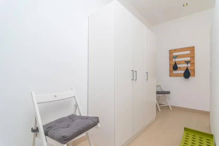A bright room with white storage cabinets, a folding chair, and wall hooks.