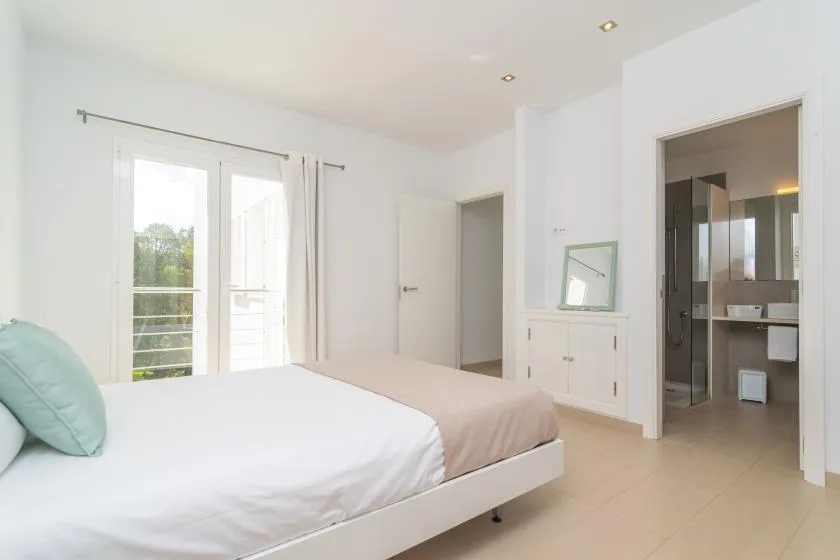 A bright bedroom with a bed, curtained glass doors, and an adjoining bathroom.