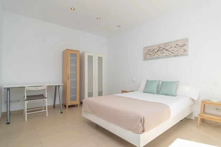 A bright bedroom with a neatly made bed and a desk beside the wardrobes.