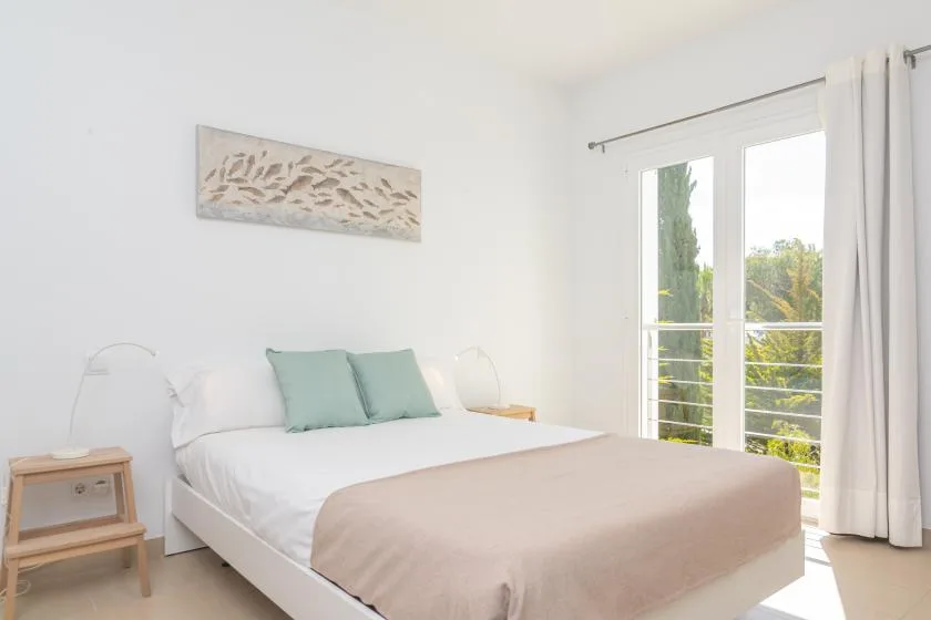A bright bedroom with a neatly made bed and pale green pillows.