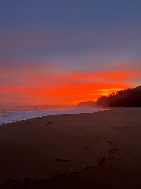 Una playa al atardecer, con olas bajo un cielo rojo anaranjado.