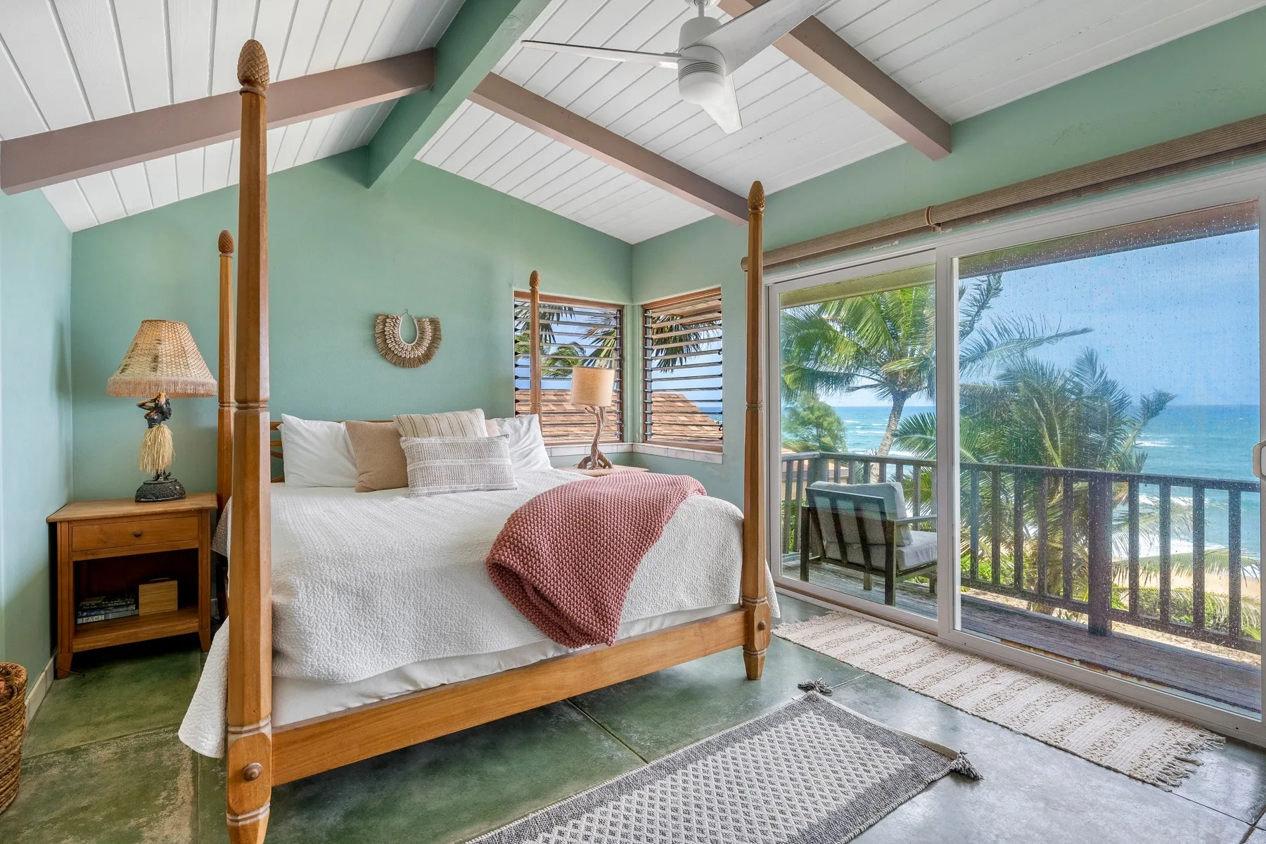 Un dormitorio con una cama de madera con dosel junto a grandes ventanas con vista al océano.