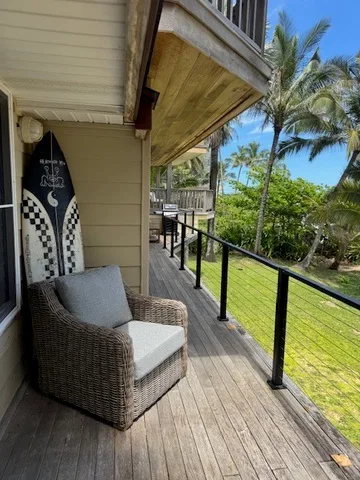 Una terraza exterior cubierta tiene asientos de mimbre junto a una barandilla y palmeras.
