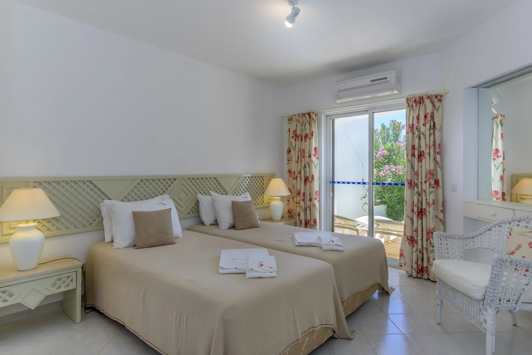 A bedroom with a large bed, bedside tables, and floral curtains by the glass doors.