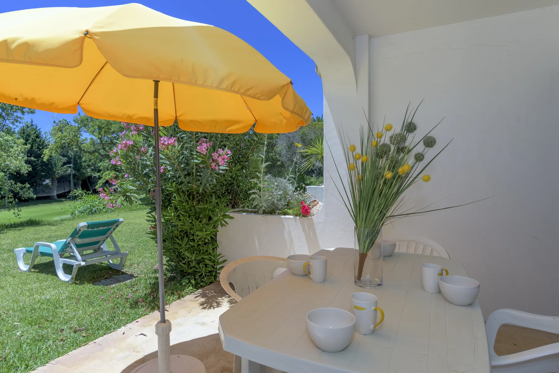 An outdoor dining area under a yellow umbrella overlooks a garden.