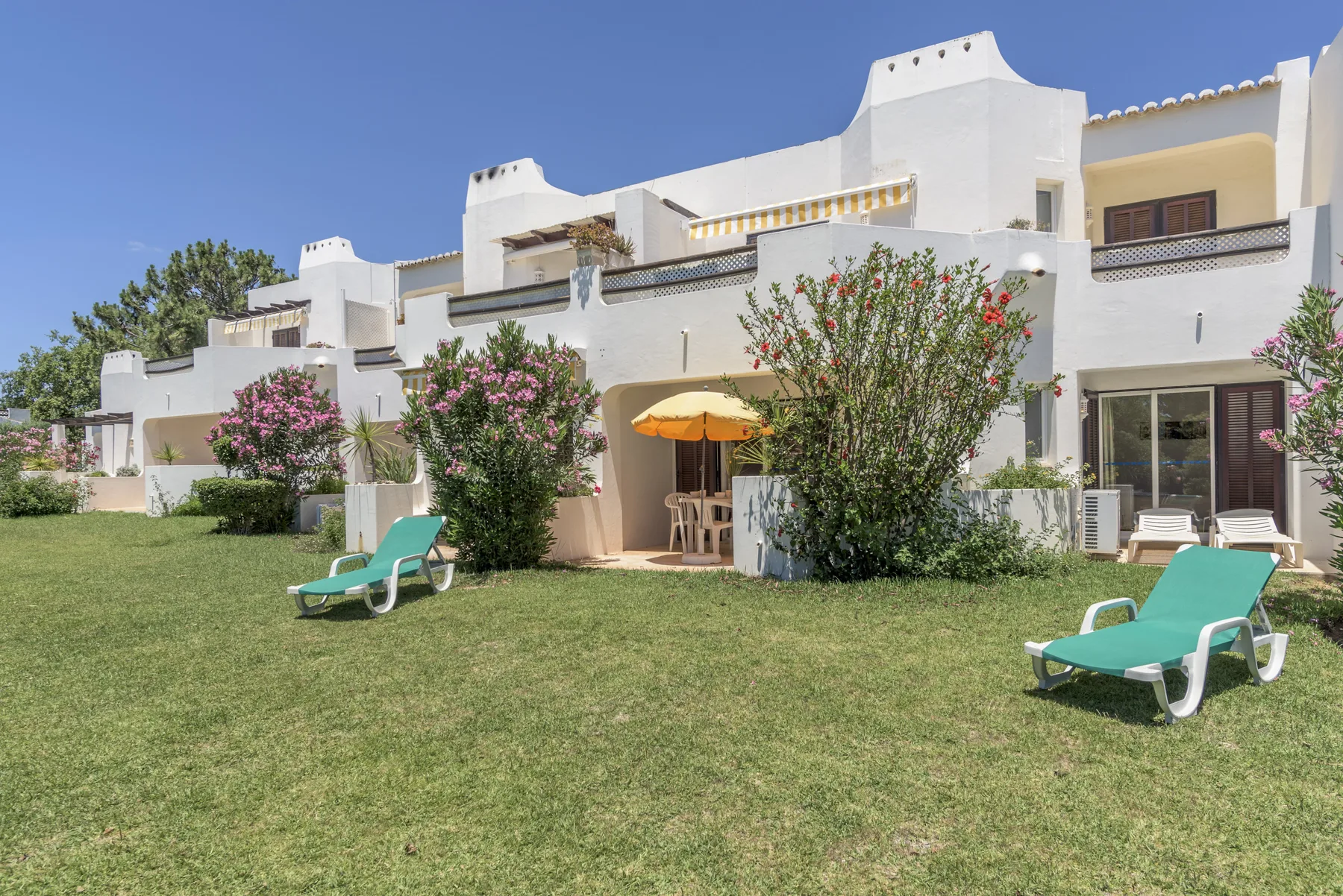 White apartment buildings line a grassy courtyard with lounge seating and flowering shrubs.