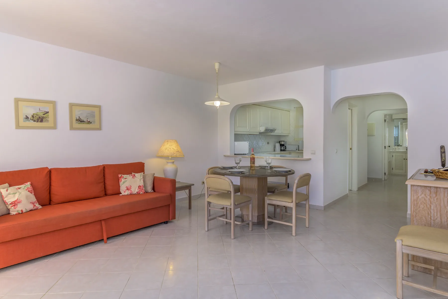 A living and dining area with orange seating beside a small kitchen.