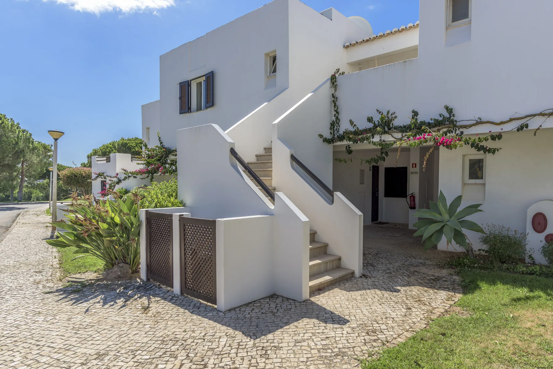 White residential buildings with an exterior staircase and a paved courtyard.