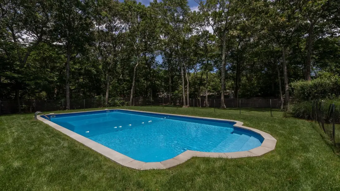 Una piscina está en un claro cubierto de césped y rodeado de árboles.