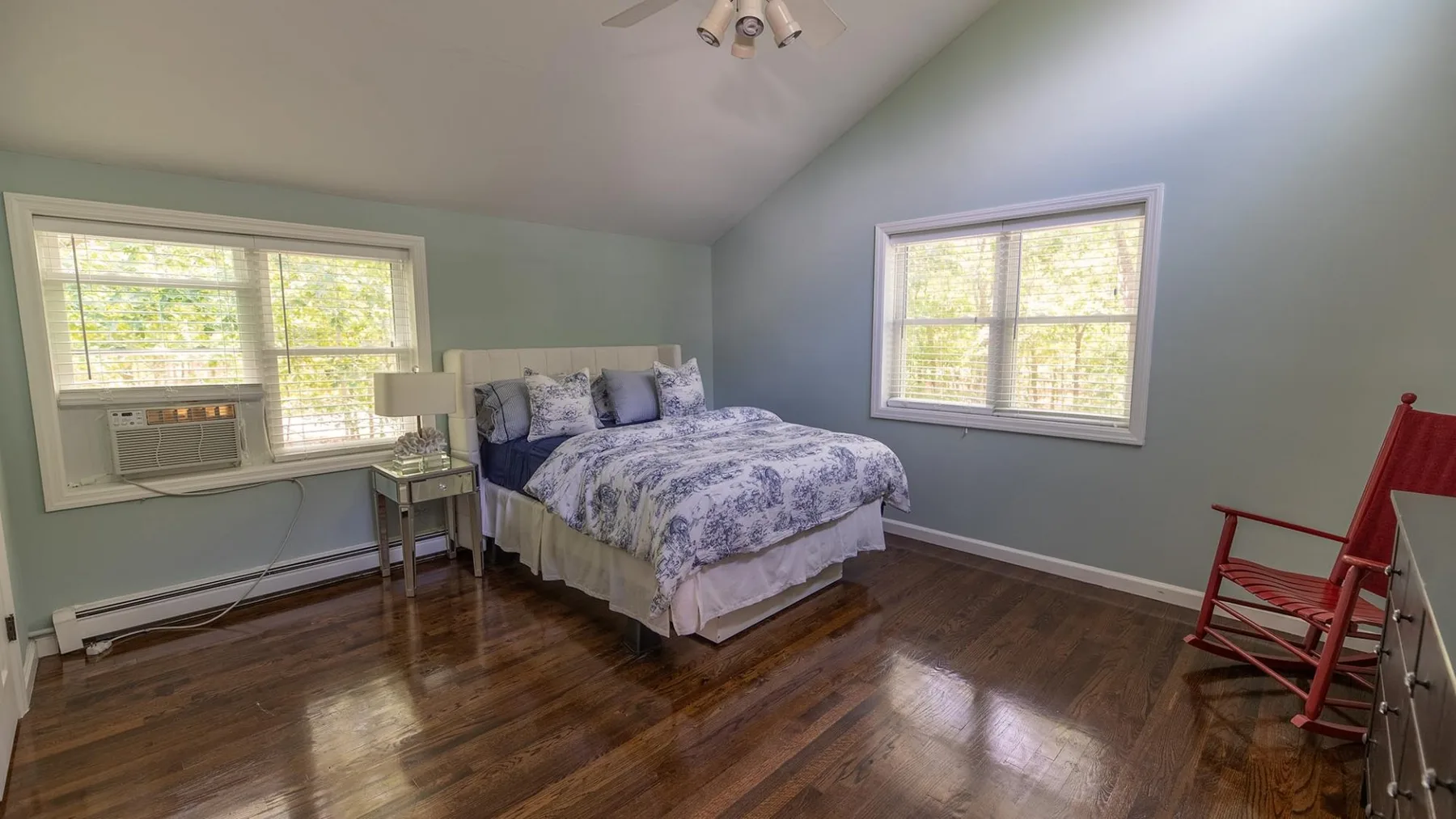 Un dormitorio con una cama, ventanas y una mecedora de madera.