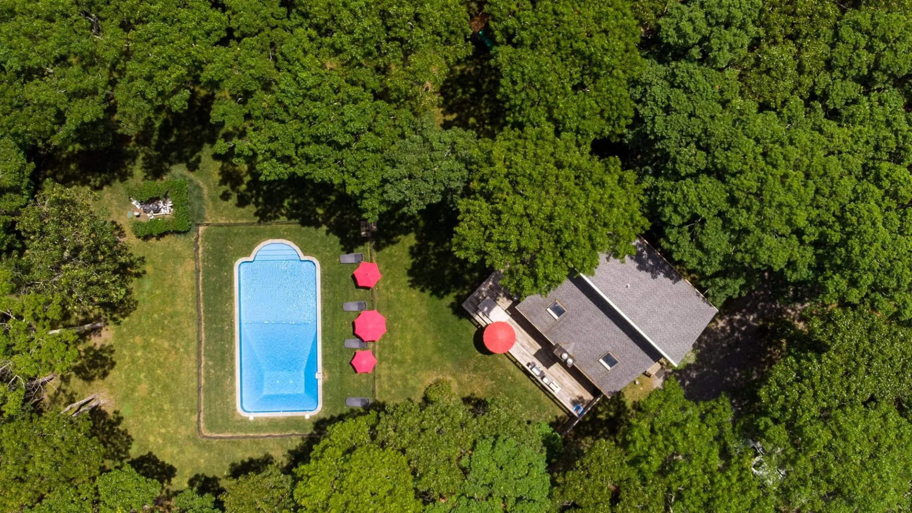 Una vista aérea muestra una casa junto a una piscina, rodeada de árboles.