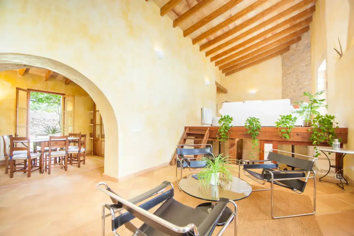 A bright living area with seating, a glass coffee table, and a dining area beyond an archway.