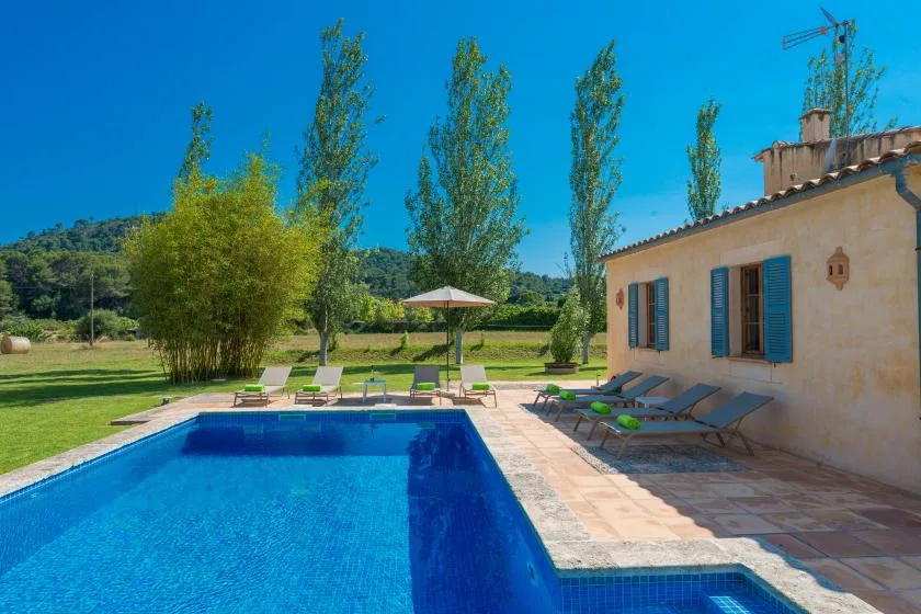 A swimming pool beside a light-colored house, with lounge chairs on the patio.