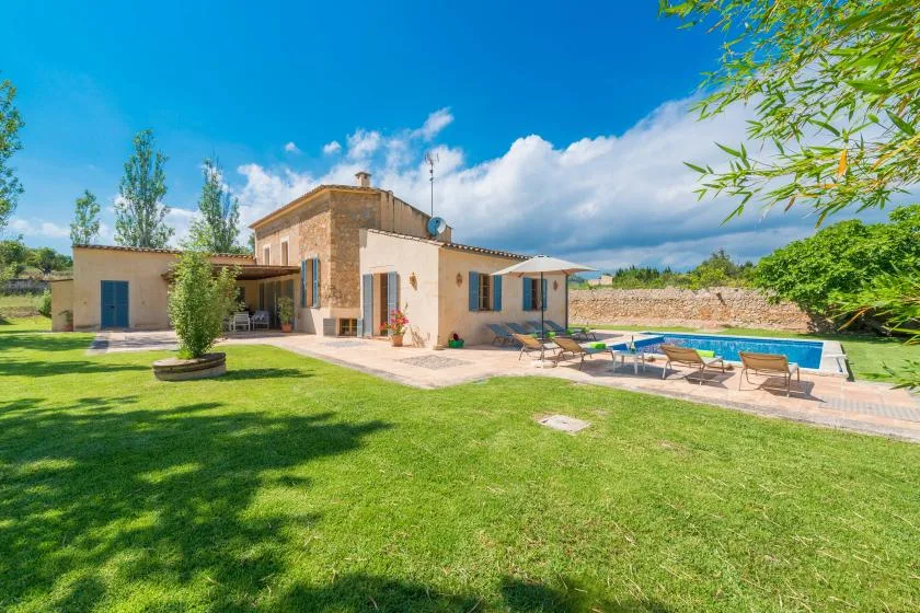 A house and swimming pool sit beside a broad lawn under a blue sky.