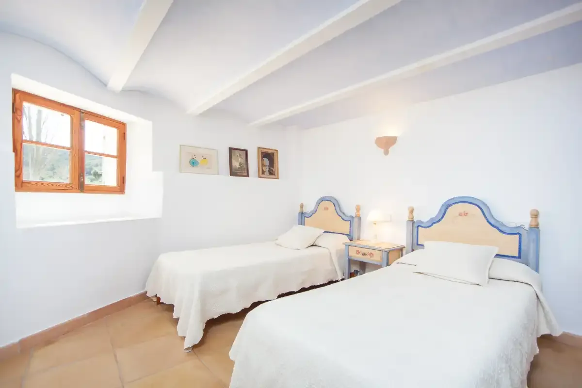 A bright bedroom with two beds and a window.