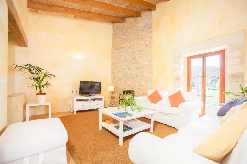 A bright living room with white seating, a coffee table, and a television.