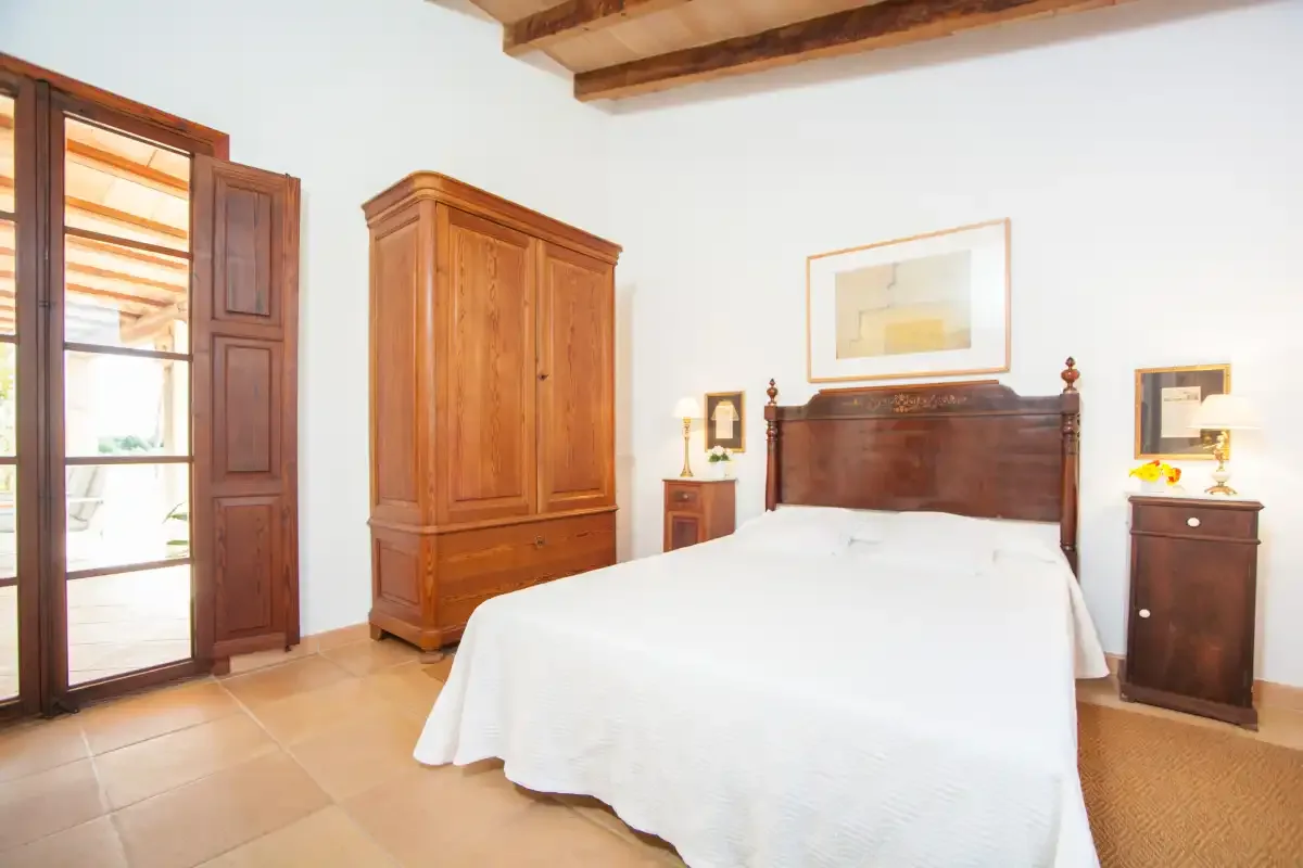 A bedroom with a large bed, wooden wardrobe, and tall windows.