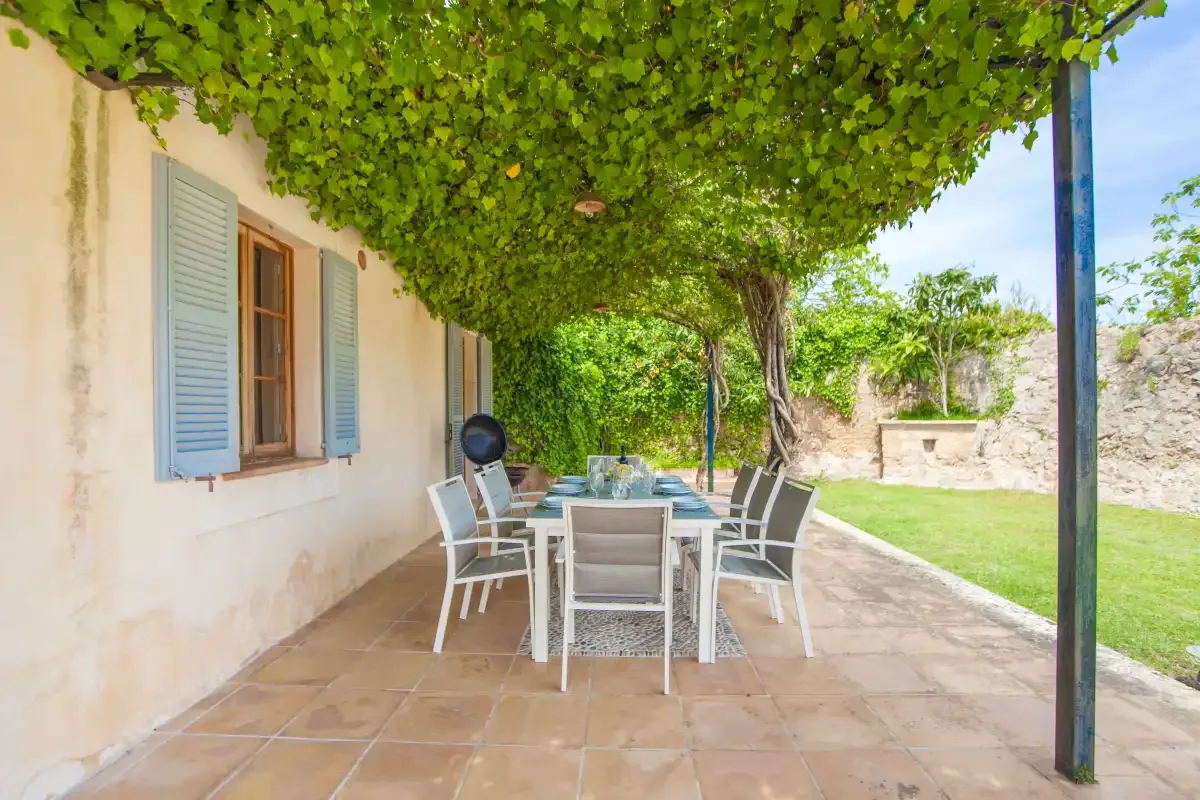 A shaded outdoor dining area with a table and seating beside the house.