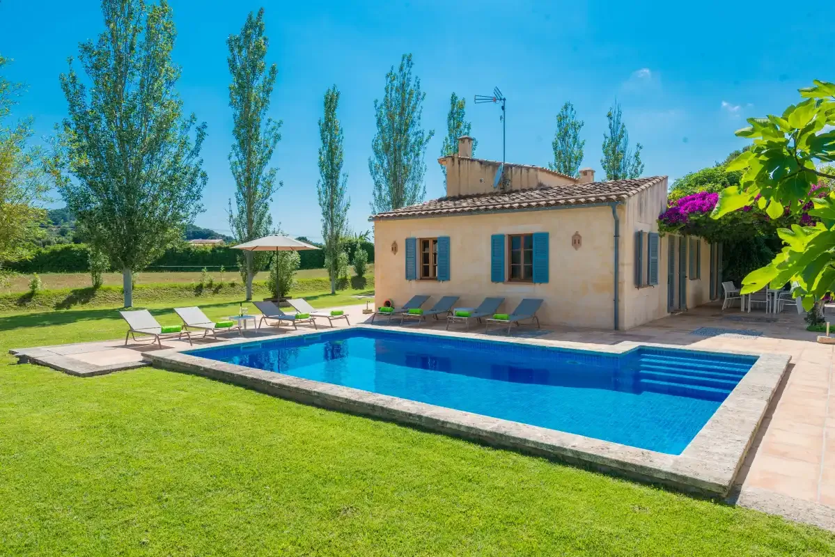 A swimming pool sits beside a house, with lounge seating and a grassy yard.