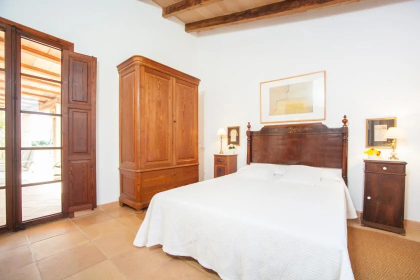 A bedroom with a large bed, wooden wardrobe, and open shutters.