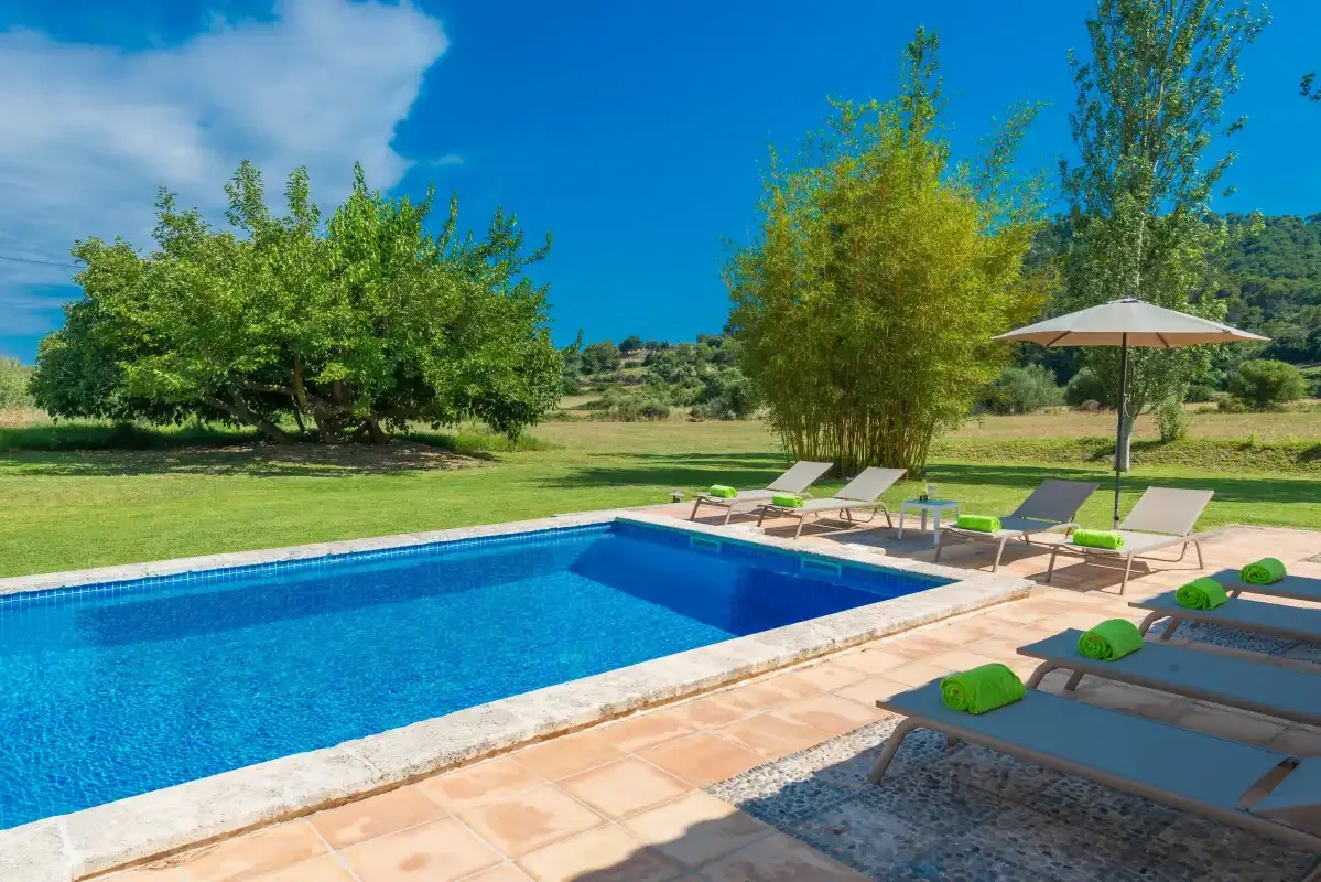 An outdoor swimming pool beside a lawn, with sun loungers and an umbrella.